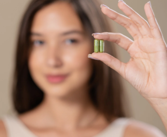 Kobieta trzymająca w ręce kapsułki leku.